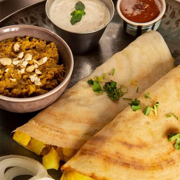 Two golden-brown Sri Balaji dosas filled with potatoes, served with chutney, sambar, and onions.